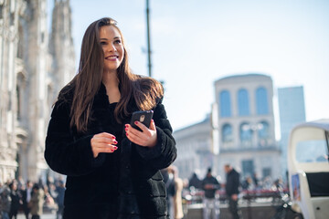 Obraz premium Woman using her smartphone while walking in a city