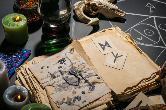 Witch's magic attributes with crystal ball of fortune teller and book on dark table, closeup