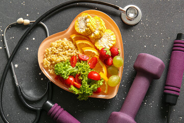 Plate with fresh healthy products, stethoscope, jumping rope and dumbbell on dark background. Diet...