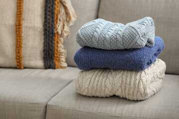 Stack of knitted sweaters on grey sofa, closeup