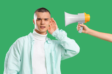 Teenage boy trying to hear something and hand with megaphone on green background