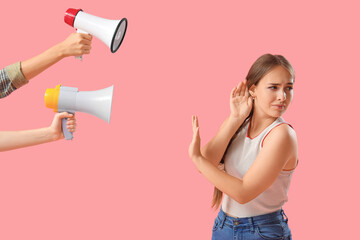 Teenage girl with hearing problem and megaphones on pink background