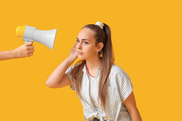 Teenage girl trying to hear something and hand with megaphone on yellow background
