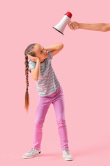 Little girl suffering from noise and hand with megaphone on pink background