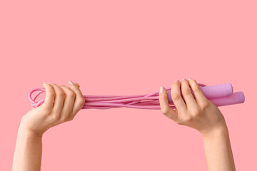 Female hands with skipping rope on pink background