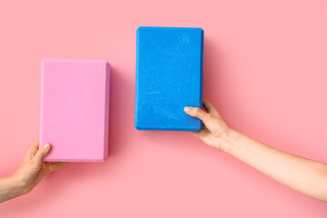 Female hands with yoga blocks on pink background