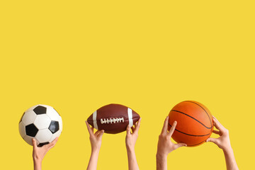 Female hands with sports balls on yellow background