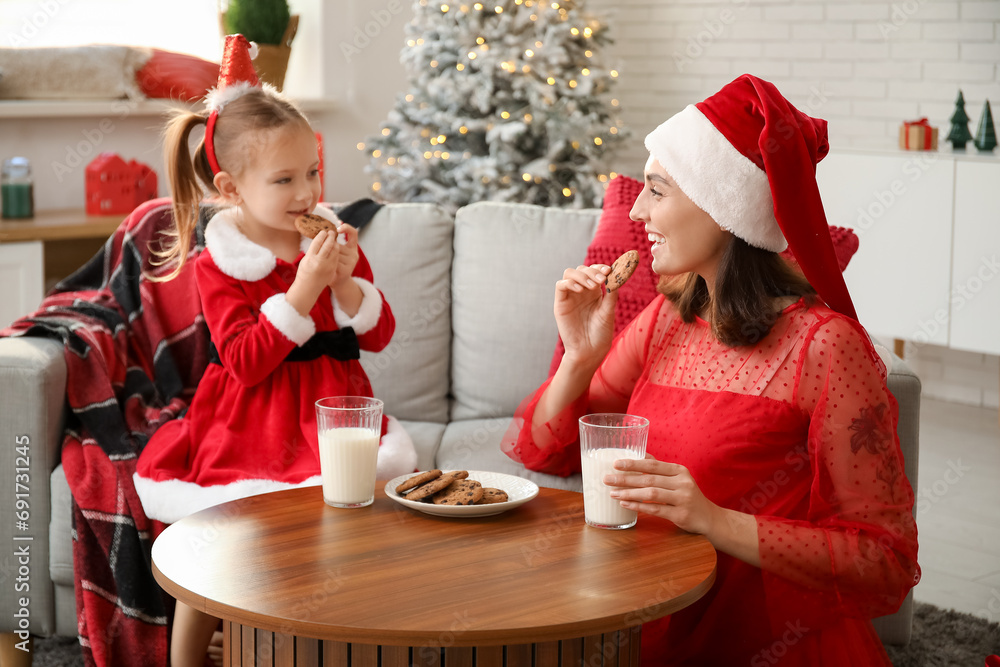 Sticker Happy mother with her little daughter eating cookies with milk at home on Christmas eve