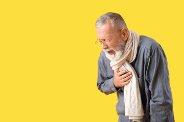 Sick mature man in scarf sneezing on yellow background