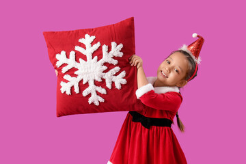 Cute little girl in Santa Claus costume with red Christmas pillow on color background