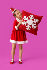 Cute little girl in Santa Claus costume with red Christmas pillow on color background