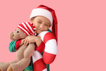 Cute little girl with teddy bear and Christmas cushion on pink background