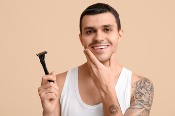 Handsome young man with razor on beige background