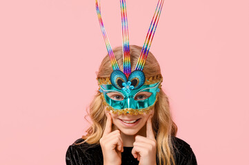 Smiling little girl wearing carnival mask on pink background