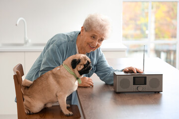 Senior woman with pug dog listening radio in kitchen