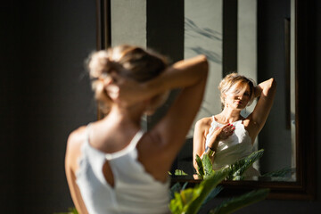 The bride in a white dress looks in the mirror and sees herself reflected in the sunlight