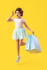 Shocked little girl with hair curlers and shopping bags jumping on yellow background