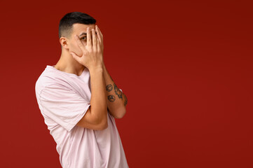 Handsome ashamed young man covering face with hands on red background
