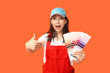 Female Asian shocked painter pointing at paint color palettes on orange background