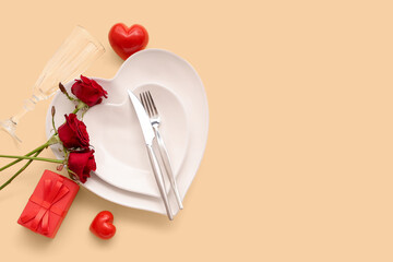 Beautiful table setting with red roses, gift box and hearts on yellow background. Valentine's Day celebration