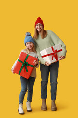 Cute little girl and her mother with Christmas gift boxes on yellow background