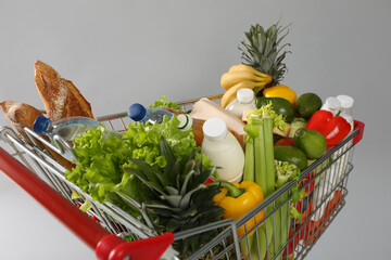 Shopping cart full of groceries on grey background