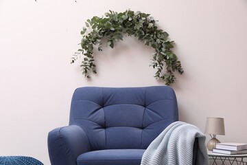 Beautiful garland made of eucalyptus branches hanging above armchair on white wall indoors