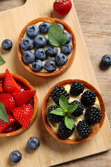 Tartlets with different fresh berries on wooden table, flat lay. Delicious dessert