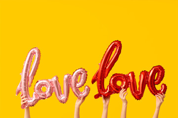 Female hands with air balloons in shape of word LOVE on yellow background. Valentine's Day celebration