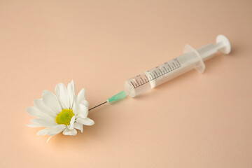Medical syringe and beautiful chrysanthemum flower on beige background, closeup