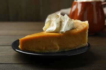 Piece of delicious pumpkin pie with whipped cream on wooden table, closeup