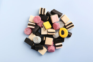 Many tasty liquorice candies on light blue background, top view