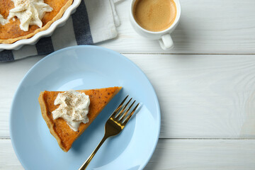 Delicious pumpkin pie with whipped cream, fork and cup of coffee on white wooden table, flat lay. Space for text