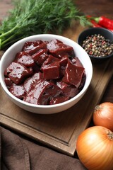 Cut raw beef liver with onions, dill and spices on wooden table