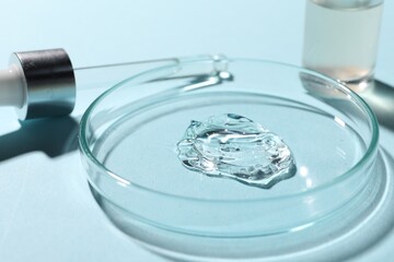 Bottle of cosmetic serum and petri dish with sample on light blue background, closeup