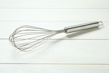 Metal whisk on white wooden table, closeup