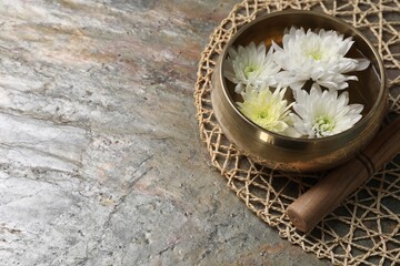 Tibetan singing bowl with water, beautiful chrysanthemum flowers and mallet on table, space for text