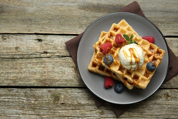 Delicious Belgian waffles with ice cream, berries and caramel sauce on wooden table, top view....