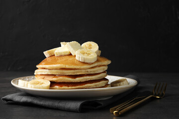 Delicious pancakes with bananas, butter and honey on dark table. Space for text