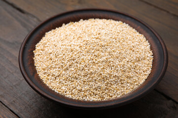 Raw barley groats in bowl on wooden table, closeup
