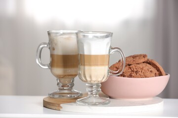 Aromatic latte macchiato in glasses and chocolate cookies on white table against light background