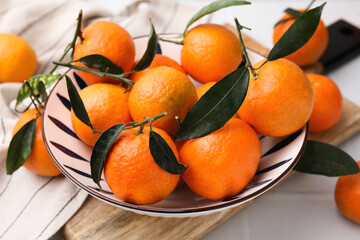 Fresh ripe tangerines with green leaves in bowl on white table, closeup