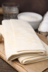 Raw puff pastry dough on wooden table, closeup