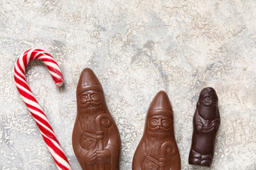 Chocolate Santa Clauses and candy cane on grunge background, closeup