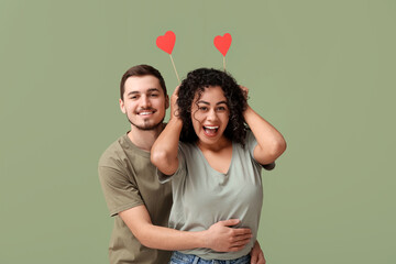 Funny young couple with paper hearts for Valentine's day on green background