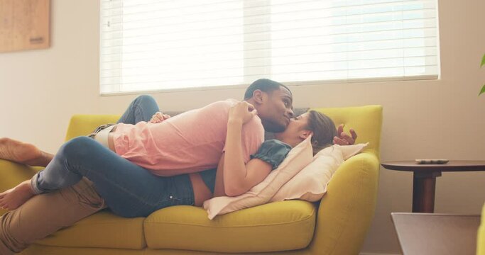 Attractive young millennial couple hold each other on the couch in their new apartment. Happy African American and Caucasian man and woman in love as they move in together. 4k slow motion handheld