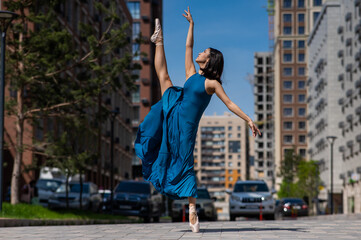 Beautiful Asian ballerina in blue dress posing in splits outdoors. Urban landscape.