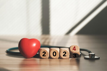 Happy New Year 2024, stay healthy, family insurance. The image consists of a wooden block with the word 2024 and a stethoscope with a red heart. There is space to enter text. - Powered by Adobe