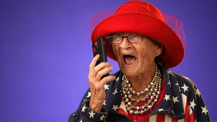 Closeup of toothless funny old grandmother wearing glasses US flag jacket isolated on purple background talking on phone. Concept portrait of crazy senior youthful woman.