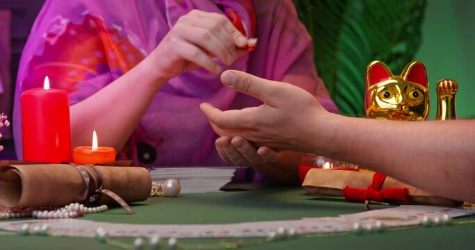 Esoteric ritual of chakra opening, energy protection with talisman stone fortune teller runs red crystal over client hand, drawing lines on palm Salon of astrology, fortune telling with tarot cards